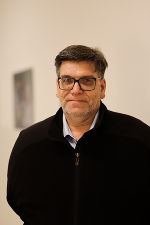 Person mit dunklem Jackett und Brille blickt in die Kamera.
