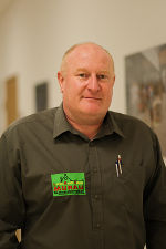 Person mit olivgrünem Hemd und Namensschild, freundlicher Gesichtsausdruck.